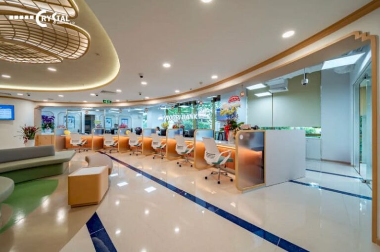 Nội thất ngân hàng hiện đại với quầy giao dịch màu vàng nhạt, ghế trắng xoay, sàn đá trắng kẻ sọc xanh và khu vực chờ với sofa màu xanh lá cây.