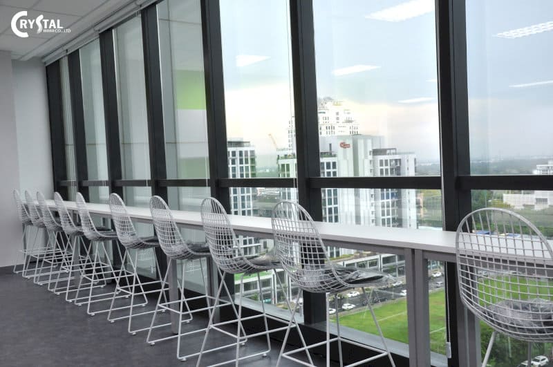 Khu vực làm việc cạnh cửa sổ kính lớn với tầm nhìn thành phố tại Eco Kanvas Soho Suites, trang bị bàn dài trắng và ghế lưới kim loại