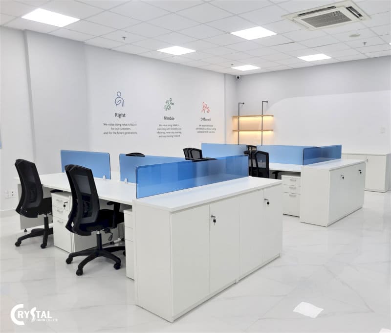 Văn phòng làm việc sáng sủa với bàn trắng hiện đại, vách ngăn màu xanh dương, ghế xoay đen thoải mái và tường trang trí với các biểu tượng và khẩu hiệu.