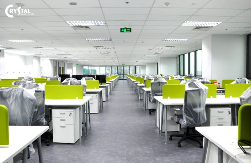 Văn phòng rộng lớn với dãy bàn làm việc màu trắng và vách ngăn màu xanh lá cây tươi sáng, nhiều ghế văn phòng bọc nilon