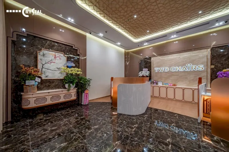 Khu vực lễ tân sang trọng của Two Chairs với sàn đá hoa cương đen bóng, quầy tiếp tân gỗ cách điệu và trang trí hoa tươi cùng tranh nghệ thuật.
