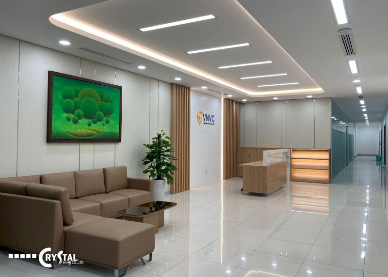 Khu vực sảnh chờ văn phòng VNVC với sofa nâu, tranh treo tường xanh và quầy lễ tân hiện đại.