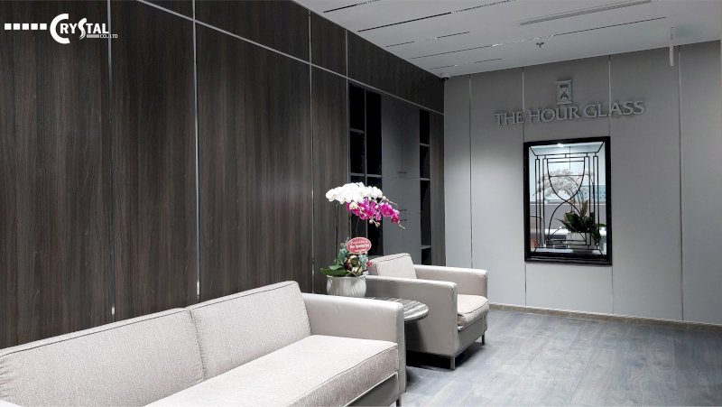 Sảnh chờ sang trọng với sofa xám, vách ốp gỗ tối màu và trang trí hoa lan tại văn phòng The Hour Glass.