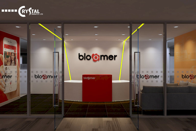 Sảnh lễ tân Bloomer hiện đại và nổi bật với logo lớn màu đen trên nền trắng, quầy lễ tân màu đỏ và trắng, cùng logo CRYSTAL ở góc trên bên trái.