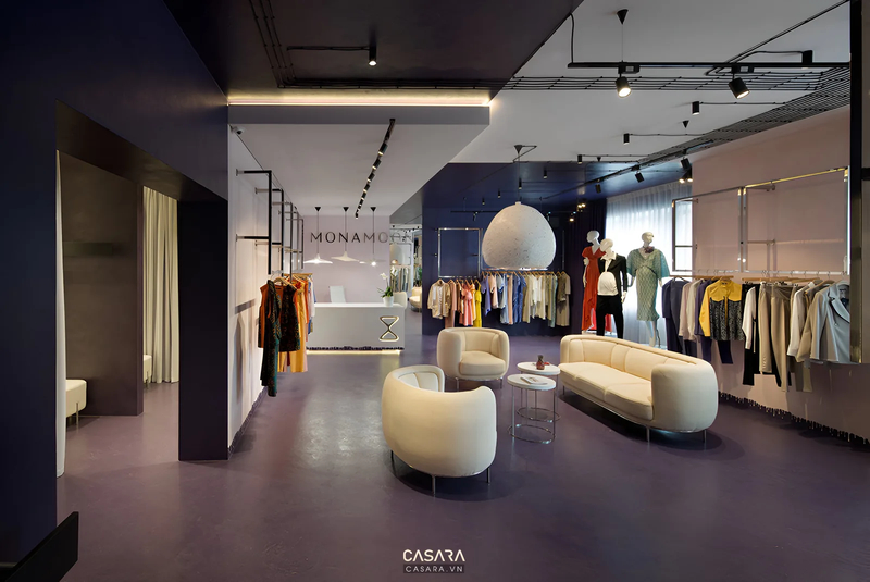 Showroom thời trang hiện đại, sang trọng với các giá treo quần áo, khu vực tiếp khách có sofa và đèn trang trí độc đáo