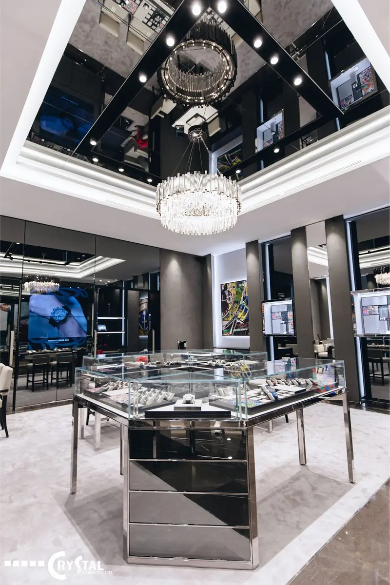 Tủ trưng bày trung tâm bằng kim loại sáng bóng và hệ trần ốp gương nhân đôi ánh sáng từ chiếc đèn chùm pha lê lộng lẫy. Thiết kế đã tạo ra một không gian ngập tràn ánh sáng và phản chiếu, mang lại trải nghiệm mua sắm xa xỉ và choáng ngợp.