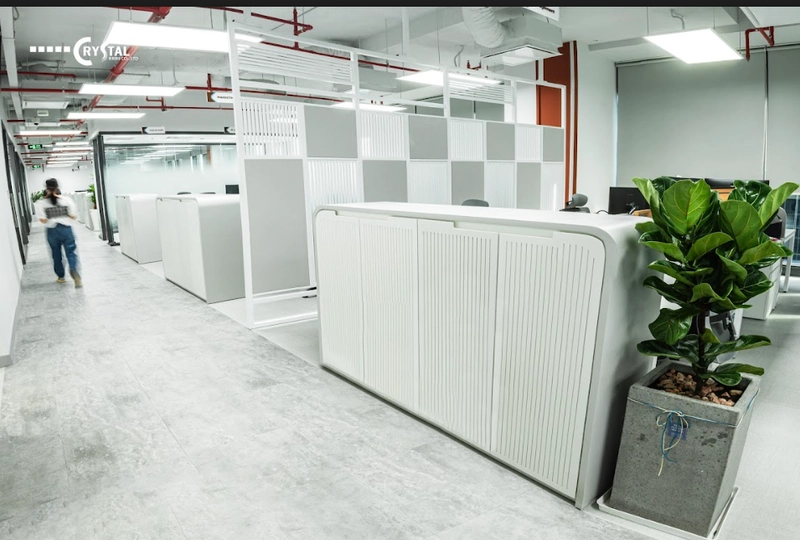 Khu làm việc open space với bàn modular bố trí linh hoạt, vách ngăn lửng acoustic hấp âm và cây xanh đặt rải rác tạo điểm thở (Nguồn: Deco Crystal)