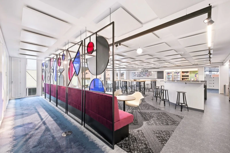 Custom steel-framed partitions with subtle colored glass inserts divide functional zones while preserving the sweeping visual transparency of the industrial envelope (Source: Internet) 