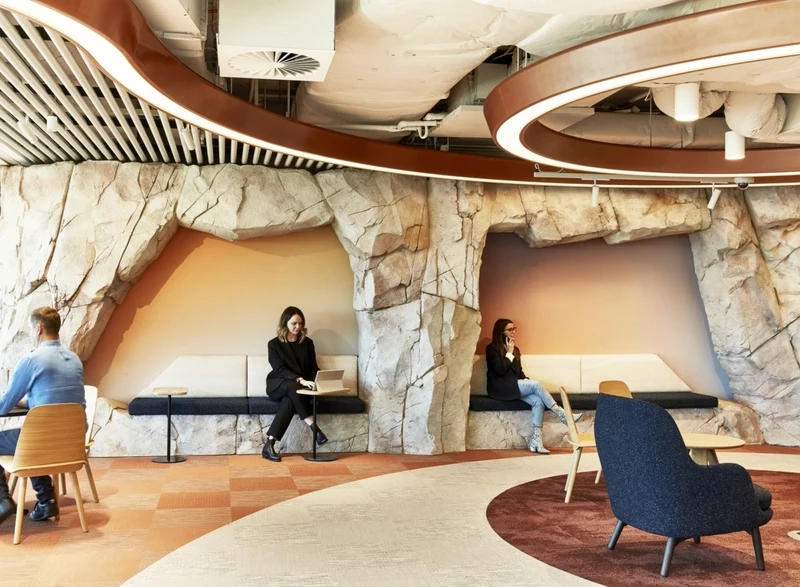 Sculpted rock formations defining intimate, warm-gradient alcoves provide a secluded yet integrated biophilic retreat against the building's spine.