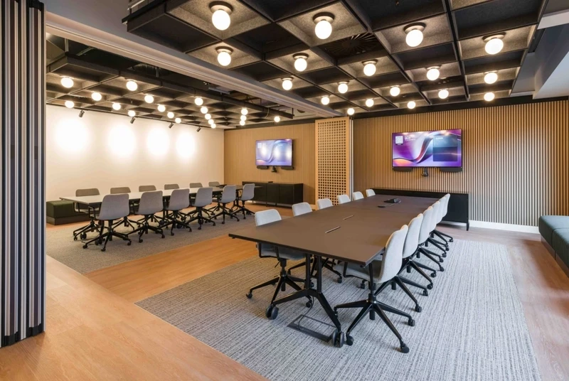 An acoustic grid ceiling and slatted timber wall panels work seamlessly to minimize echo and ensure optimal soundproofing in this modern conference space.