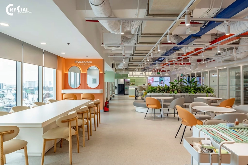 Khu pantry bàn trắng dài, ghế gỗ và gương bo tròn trên tường cam, mẫu nội thất văn phòng nhiều màu sắc