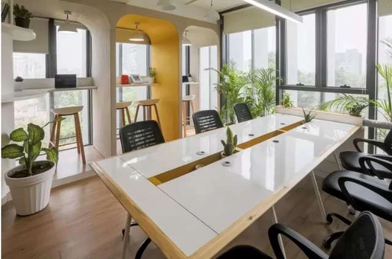 Bàn dài dùng chung và vòm tường vàng bên dãy cửa sổ lớn của một văn phòng 70m2